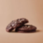 Three chocolate cookies with white chips on a light brown background; one cookie is partially eaten, creating a cozy, inviting mood.