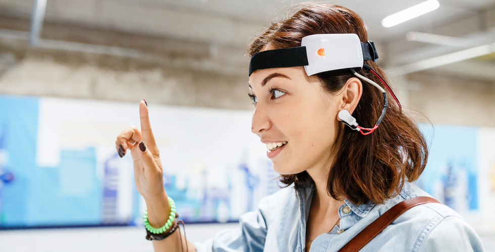A woman wearing a sensory device around her head and finger pointing in the air to a space in front of her