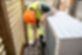A male electrician installing a heat pump in a garden on a sunny day