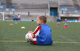 Young boy holding onto a football, while sitting on the grass