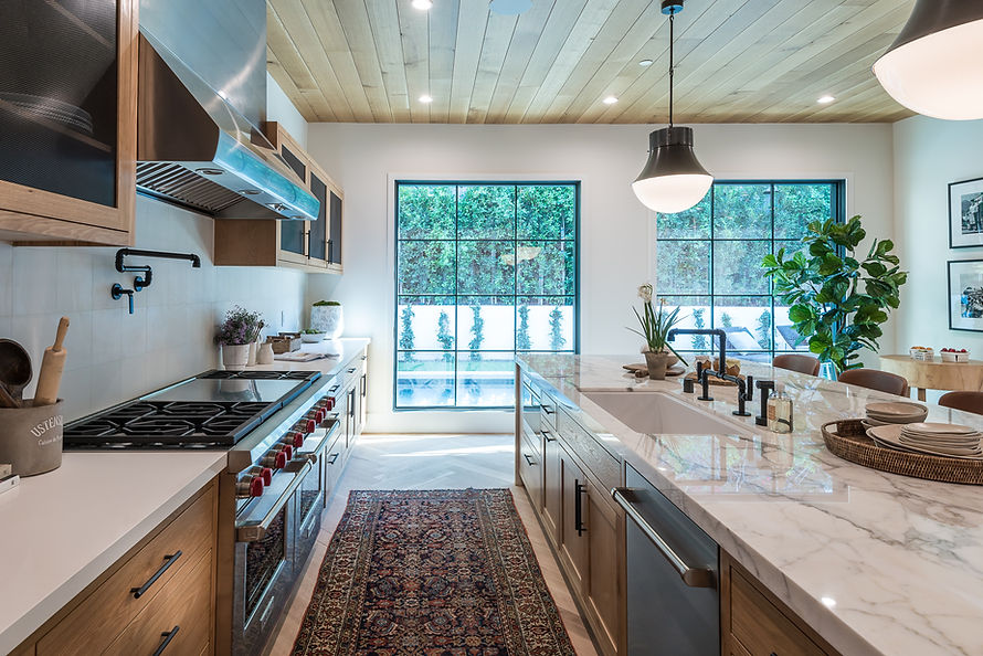 Modern kitchen with marble countertop, gas range, and a lush plant corner, framing the outdoor patio view.