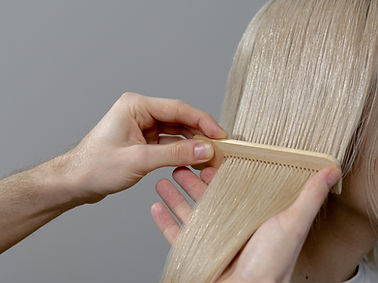 Blondes langes glänzendes Haar wird mit einem Holzkamm gestrählt.