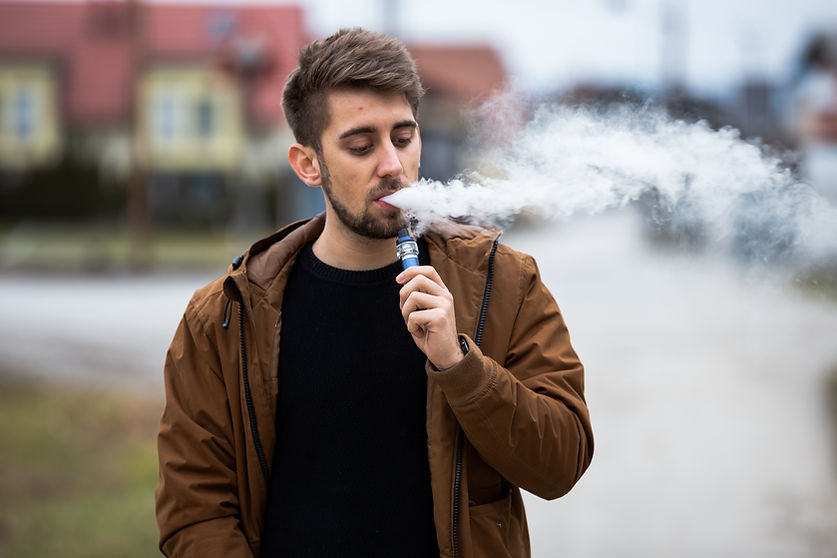 Homme vapotant avec une cigarette électronique moderne dans un environnement urbain.
