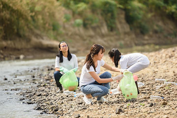 Three women picking trash at a river bank