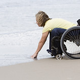 A person in a wheelchair leaning forward to put their hands in the sea