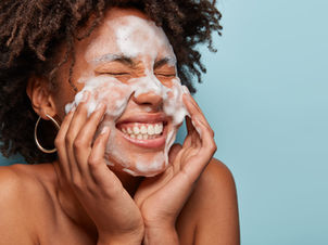 Woman laughing as she washes her face in front of a blue background