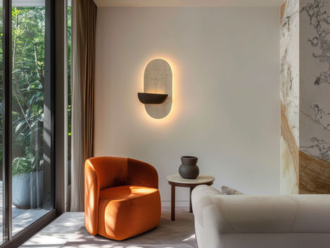 Modern living room with an orange chair, beige sofa, and round table with a vase. Illuminated wall art and large windows show greenery outside.
