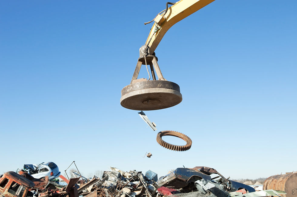 "Scrap metal is dropping from a salvage yard magnet onto a pile. Focus is on the magnet, t