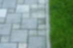 A close-up of grey patio pavers of varying sizes next to a strip of vibrant green grass
