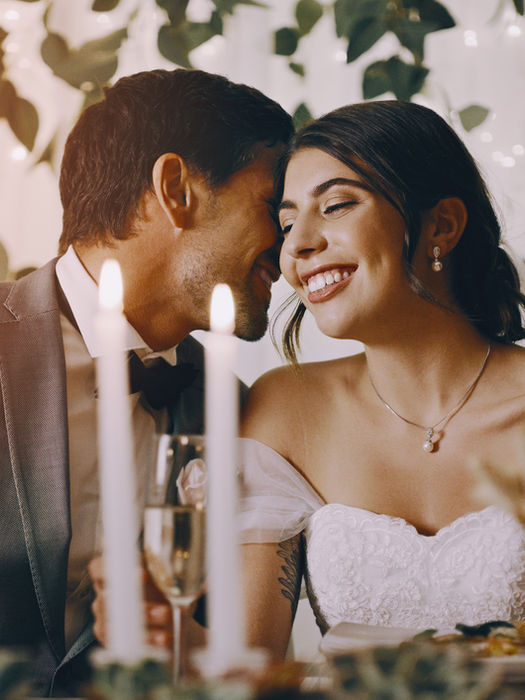 Groom whispers to happy bride at romantic wedding reception table.