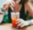 A young woman sipping a colorful cocktail through a straw, enjoying a relaxed moment at a vibrant vegan restaurant