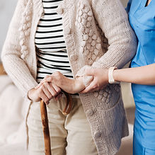 A nurse is supporting an elderly woman by holding her wrist and back.