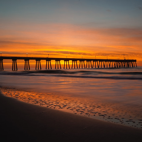 A beach with a long bridge at sunset
