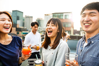 Alumni gather on a rooftop, sharing laughter and drinks as they reminisce about their university days amidst a cityscape backdrop.