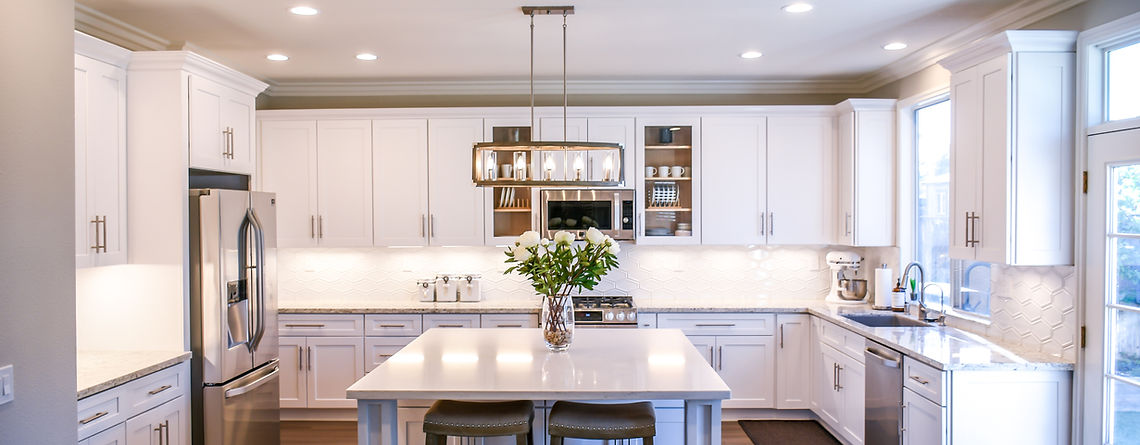 Modern coastal kitchen with a bright and airy atmosphere, featuring a blue-toned island that adds a pop of color to the space. White cabinets and white granite counters provide a crisp and clean backdrop, while fresh flowers arranged on the island add a touch of warmth and whimsy.