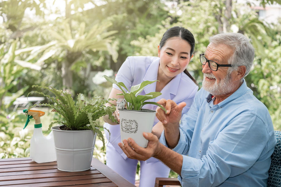 Care worker and elderly man in glasses looking at potted plants
