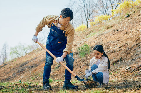 A father and daughter planting a tree on a sunny hillside.