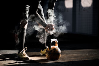 A person in athletic gear chalks their hands before lifting a kettlebell
