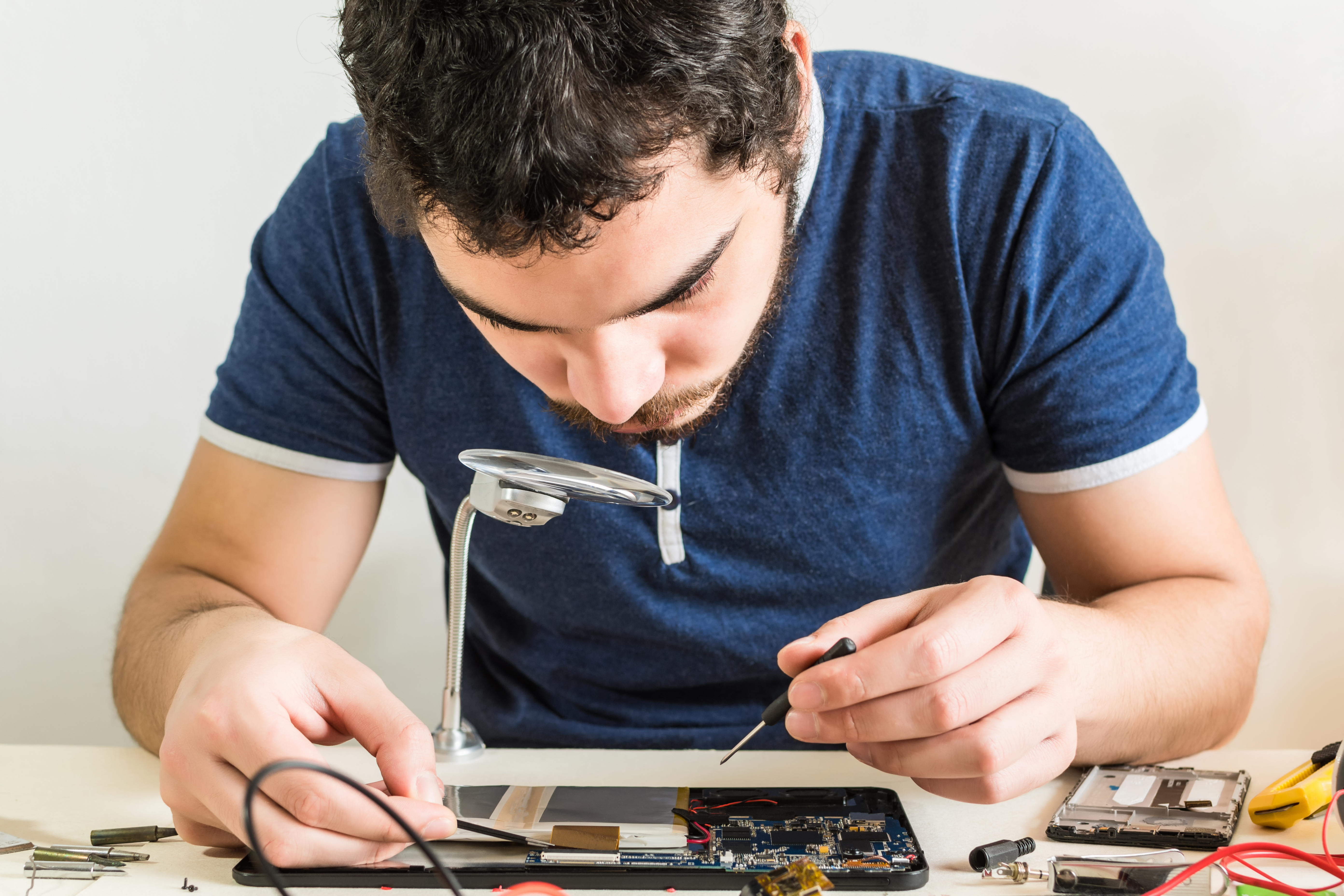 Man repairing electronic device with tools and magnifier, representing Techmave Mauritius, a tech and repair store.
