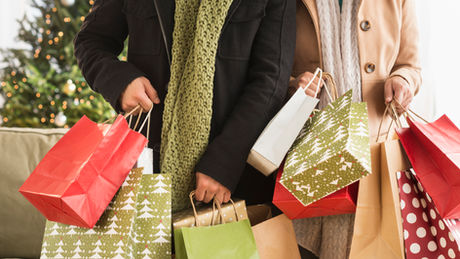 People holding festive shopping bags in a cozy setting with a decorated Christmas tree in the background. Holidays mood with vibrant colors.