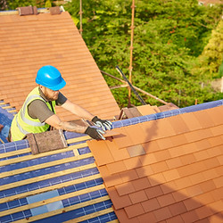 A construction worker in a helmet and safety vest installs roof tiles on a house