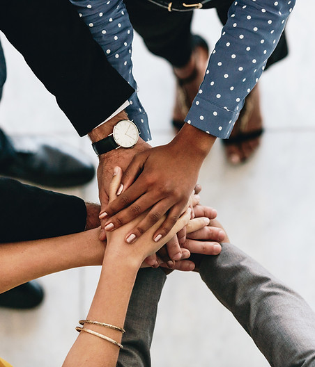 Several hands of different ethnicities coming together in the middle, on top of each other.