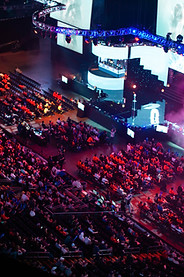 Vista aérea de un gran evento corporativo en un estadio, con una multitud de asistentes y un escenario iluminado con pantallas gigantes.juegos