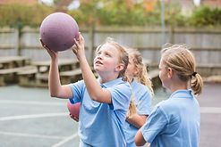 Girls in school uniform playing netball in the school yard