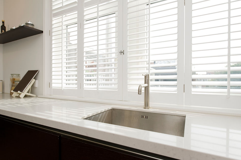 Stainless steel undermount kitchen sink beneath white plantation shutters