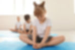 A woman assisting a young child with a seated yoga pose on a mat in a bright studio.