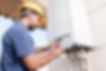 A man in a yellow hard hat and blue shirt is adjusting settings on a boiler