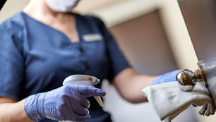 Close-up of a hotel staff member wearing gloves and a mask, disinfecting a door handle with a cloth and spray bottle, highlighting hygiene and safety measures.