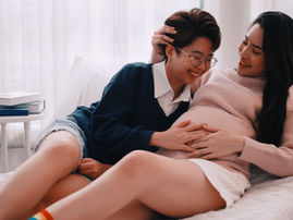 A pregnant lesbian couple cuddling on a couch