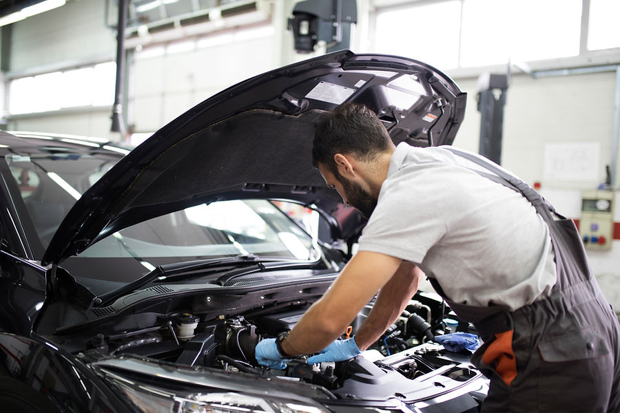 A mechanic is leaning over to work on a car's open engine