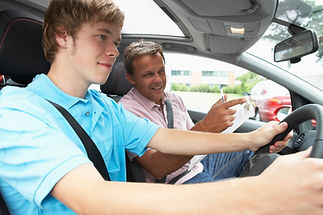 A teen boy driving a car with a male instructor next to him