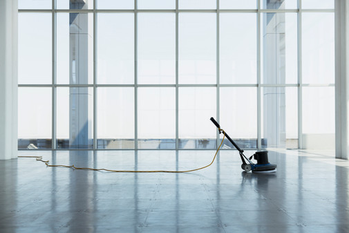 Floor polisher cleaning a shiny floor in a modern, light-filled office space.