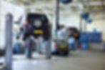 Three black cars stand in small service station and two men repair one car