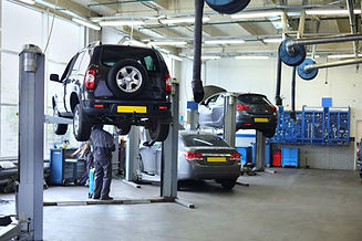 Three black cars stand in small service station and two men repair one car