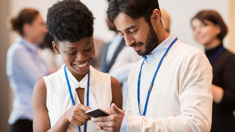 Two people smiling, engaged with a smartphone at a conference. They're wearing name badges in a bright, friendly setting.