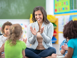 Teacher clapping in front of children sitting on floor