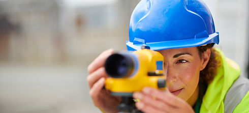 Female surveyor in a blue hard hat and hi-vis vest using a yellow digital theodolite on site