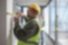 A construction worker in a yellow hard hat and vest measures a wall