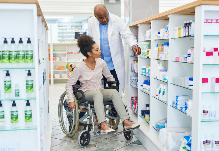 Pharmacist assisting woman in wheelchair, looking at the medication shelves