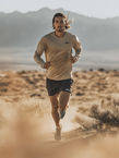 Runner in beige shirt and shorts runs through desert terrain on a sunny day