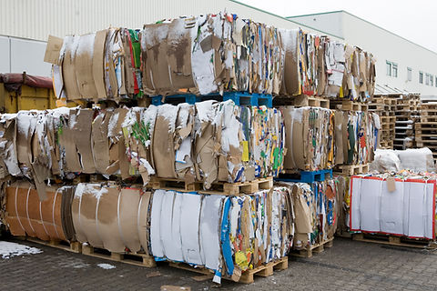 Large compressed bales of recycled cardboard stacked on wooden pallets outdoors with a dusting of snow