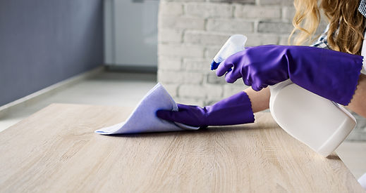 Closeup of woman's hand cleaning a wooden table, uses rag and cleaning fluid in a spray