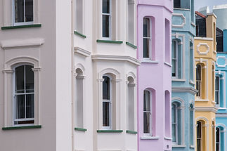 Colorful Victorian-style row houses with arched windows in pastel shades of beige, pink, blue, and yellow