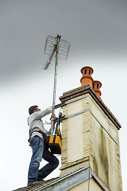 Man on roof fixing aerial to chimney