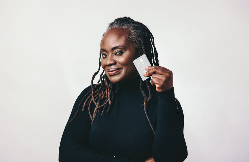 Uma mulher negra com dread no cabelo sorrindo e segurando um cartão de crédito próximo ao seu rosto