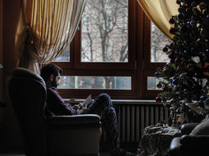 Personne assise près d’une fenêtre durant l’hiver, regard pensif. Cette image évoque la solitude, la nostalgie et les difficultés émotionnelles fréquentes pendant le temps des fêtes.